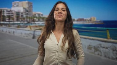 Kadın, deniz kenarındaki korkuluklara işaret ediyor. Çıplak el ve dışarıda dururken rahat duruş; kendine güven..