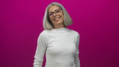 Kadın gülümsüyor ve elinde iki parmak ile mor stüdyoda barış işareti tutuyor, beyaz bluz ve gözlük takıyor; neşe;.