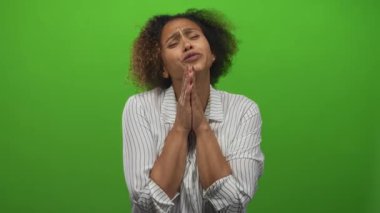 Stüdyoda elini sıkan ve gözlerini kapatan parlak yeşil ekranda dua eden bir kadın, umut diliyor..