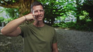 Büyük bir ağacın yanında, gözlük takan ve kolları kıvrılmış zeytin yeşili tişört giyen bir adam burun buruna;.