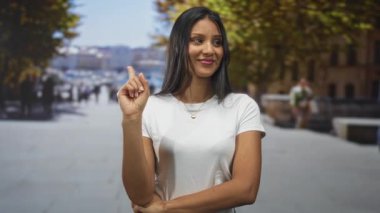 Genç esmer kadın işaret parmağı yukarı beyaz t-shirt ile sokakta yukarı doğru; güven ve özgüven.