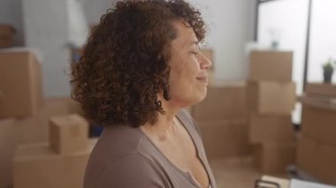 Gülümseyen kadın, yeni binadaki istiflenmiş karton kutular arasında kollarını esneterek geriye yaslanıyor..