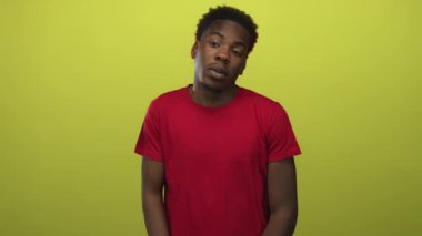Kırmızı tişörtlü bir adam yeşil stüdyoda başıyla nötr bakışlar ve hafif vücut eğikliği ile; sessiz kayıtsızlık tefekkür.
