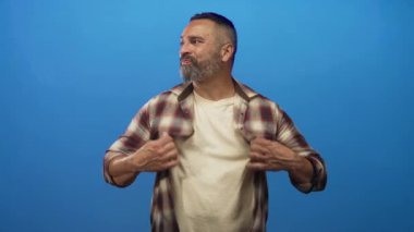 Orta yaşlı bir adam, stüdyoda elleri mavi arka planda olan ekose gömleği tutuyor..