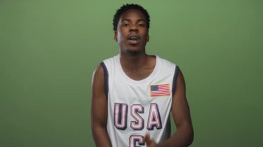 Young african american man smiling extends hand wearing usa jersey in green studio; welcome trust unity.