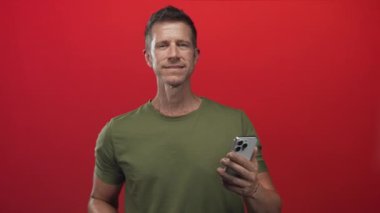 Bilekliklerle kırmızı bir stüdyoda akıllı telefon tutan ve orta parmağını kameraya doğru uzatan bir adam..