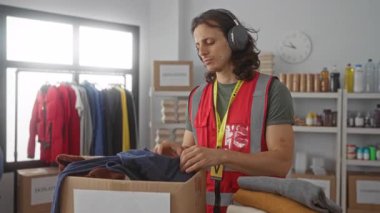 Kırmızı güvenlik yeleği giyerken bir süveter katlayan ve bağış merkezindeki bağışları sıralayan bir adam; kamu hizmeti şefkati.