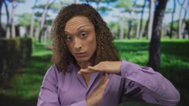 Kadın, uzun çam ağaçları ve manikürlü çitlerle güneş ışığı altında yemyeşil parkta el ele tutuşup kendine güveni durduruyor..