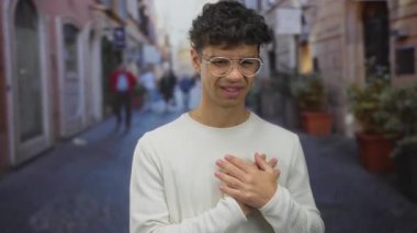 Kalabalık şehir caddesinde yuvarlak gözlüklü ve beyaz kazaklı bir adam el ele tutuşuyor..