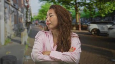 Sokakta kollarını kavuşturmuş, dudaklarını büzmüş bir kadın park etmiş arabaların ve şehir ağaçlarının yanında hayal kırıklığı bekliyor..