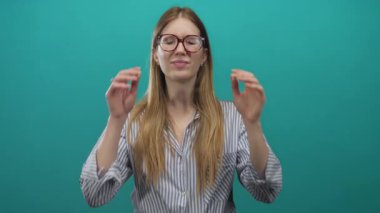 Çizgili gömlekli genç sarışın kadın gözlerini kapatır ve iki eliyle deniz mavisi bir stüdyoda gözlük ayarlar..