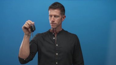 Mavi stüdyoda elinde araba anahtarı olan siyah gömlek ve bileklik takan bir adam. Sürpriz yeni araba..