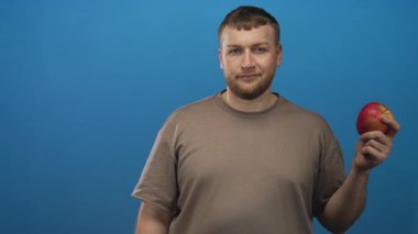 Kırmızı elmayı tutan ve mavi stüdyoda gülümseyen bir adam; arkadaşça sağlıklı atıştırmalık promosyonu.