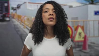 Sarı bariyerler ve kamyonlarla dolu bir inşaat alanında kadın keskin bir şekilde ağzından nefes veriyor..