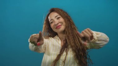 Stüdyoda gülümseyen yüz ve parmaklarını gösteren iki parmağıyla kamerayı gösteren bir kadın..