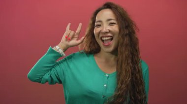 Pembe stüdyoda elleri ve kırmızı tırnakları olan, yeşil kazaklı ve uzun saçlı bir kadın..