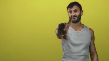 Adam sarı stüdyodaki kameraya işaret parmağıyla işaret ediyor gri askılı ve sakallı, önden poz veriyor; sert uyarı.