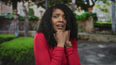 Orman yolunda çene altına yumruk atan, yeşil çalılar ve yosunlu taşlarla kaplanmış kırmızı bluzlu bir kadın..