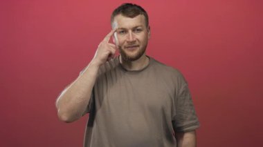 Erkekler şakağı işaret eder ve stüdyoda kahverengi tişört giyerek kırmızı arka plan ve hafif ışıklandırmayla gülümserler. Düşünceli bir fikir..