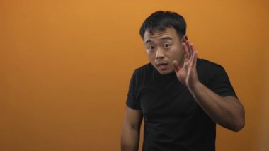 Stüdyoda genç Çinli bir adam kulağını öne eğip dikkatlice dinlemek için elini kaldırıyor..