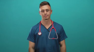 Mavi önlüklü doktor, stüdyoda görülebilen kırmızı steteskoplu pazılarını esnetiyor; kendine güven kuvveti pozu.