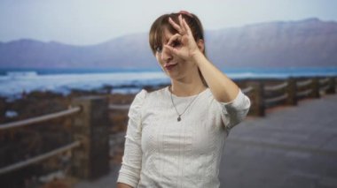 Beyaz bluzlu kadın deniz kenarındaki korkuluklarda el ele vererek daire hareketi yapıyor..