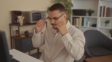 Hispanik adam ayakta otururken ve ekrana bakarken masadaki bardakları ayarlar; odaklanır.