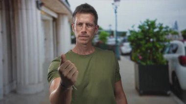 Bina ve park halindeki arabaların yanında yeşil t-shirt ve gözlük takan adam, kararlılık.