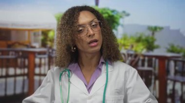 Steteskop jestleri olan beyaz önlüklü kadın doktor elleri restoran terasında; sakin denge.