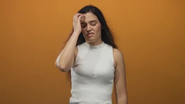 Latin kökenli genç bir kadın, elini turuncu stüdyoya sokup, beyaz kolsuz bluz giyiyor..