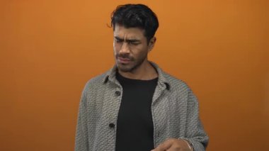 Siyah gömlek ve desenli palto giyen adam, keskin bir kokudan korkarak turuncu stüdyo ortamında burnunu çimdikliyor..