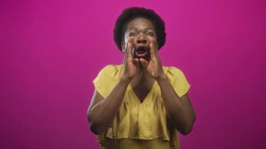 Stüdyoda, sarı bluz giyen, eflatun arkaplan karşısında el pençe divan duran kadın, animasyon ifadeli orta çekim; anlamlı neşe.