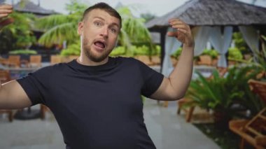 Elleri havada ve ağzı açık bir adam otel binası ve kabin sandalyelerinin yanındaki havuzda jest yapıyor. Sürpriz tatil tatili eğlencesi..