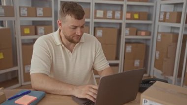 Bir adamın dizüstü bilgisayarda yazması ve bir binanın raflarındaki karton paketlerin arasında yapışkan bir nota yazması; odaklanmış üretkenlik.