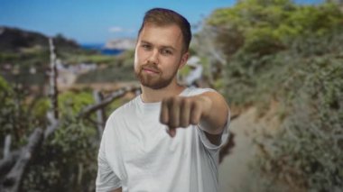 Orman yolunda beyaz t-shirt ve yumruk giyen sakallı genç adam kameraya doğru genişledi; kararlılık dayanıklılığı.