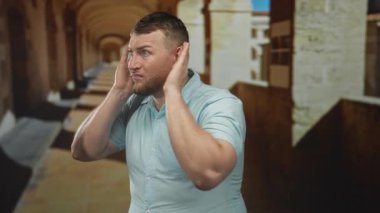 Avuç içleriyle omuz silken ve kulaklarını tıkırdatan bir adam kemerli sütunlu eski bir kasaba caddesinde, kolları açıkta ve kafası karışmış bir ifade;.