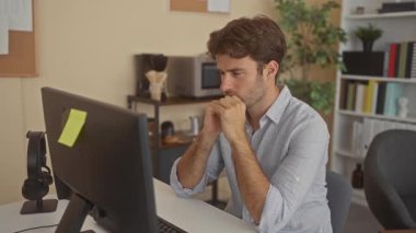 Ofis binasında elleri tapınaklarda olan bilgisayar monitöründeki genç İspanyol adam; stres yoğunlaştırma süresi.