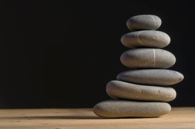 Tahta masa üzerinde dengeli altı gri taş yığını, siyah arkaplan, denge konsepti