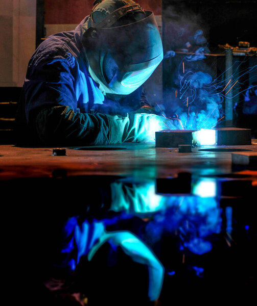 industry - welder in action with face shield, overalls and gloves