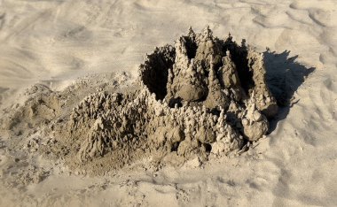 Güneşli bir sahilde kum damlalı kale heykeli, yaz eğlencesi ve yaratıcılık sergileniyor.