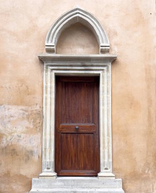 Eski bir taş kemer ve alçı duvardaki ahşap kapı tarihi bir binaya açılıyor.