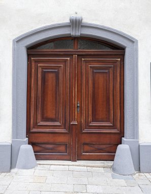 Geleneksel kahverengi ahşap kapı kemerli gri taş çerçeve ile binaya erişim sağlar.