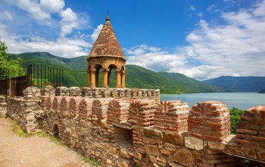 Güneşli bir günde yeşil dağlar ve Zhinvali Gölü ile tarihi Ananuri kalesi duvarı ve kulesi