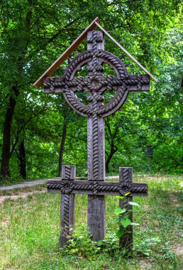 Yeşil bir orman mezarlığında el oyması ahşap bir haç duruyor.
