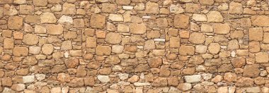 Eski taş duvar yüzeyinde çeşitli şekiller ve boyutlarda kahverengi yapı taşları var.