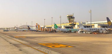 Gran Canaria, İspanya 16 Aralık 2023: Ticari yolcu uçakları arka planda kontrol kulesi olan bir havaalanı terminaline park edildi