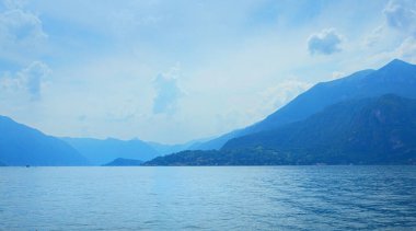 Como Gölü 'nün sakin mavi suyu, sakin bir gökyüzünün altındaki uzak İtalya sıradağlarını yansıtıyor.