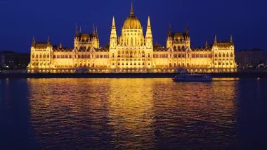 Geceleyin aydınlanan Macar parlamentosunun önündeki Tuna Nehri 'nde yelken açan turistik tekne.
