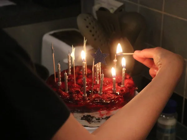 Mão segura um fósforo acende velas em um bolo vermelho — Fotografia de Stock