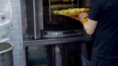İş teması üzerine bulanık odaklanmış video. Modern küçük işletme. Tanınmayan biri fırından çörek tepsisi çıkarır.